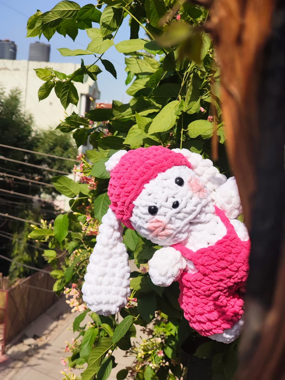 Handmade white crochet bunny plush with floppy ears, pink overalls, and a matching hat, soft amigurumi rabbit toy for home décor and gifting.