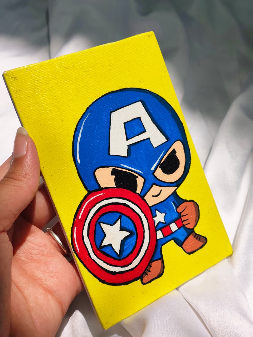 Cartoon Captain America figure on a yellow background held by a hand.