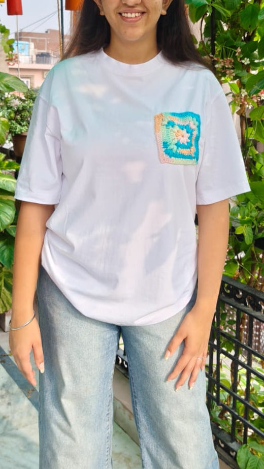 Person wearing a white t-shirt with a logo on a balcony with greenery