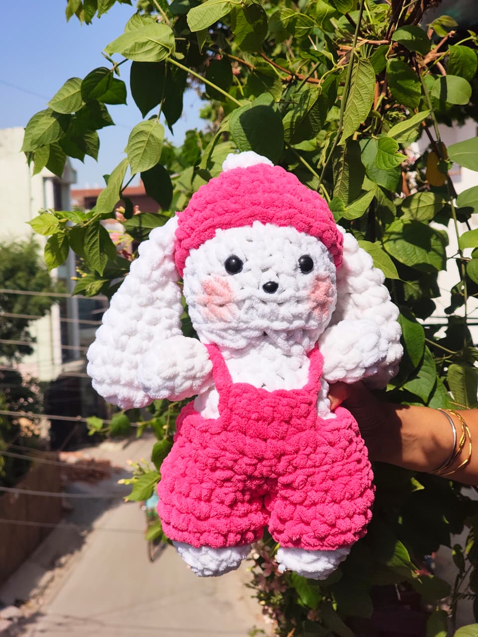 Handmade crochet bunny plush wearing pink overalls and a matching winter hat, soft amigurumi rabbit toy for nursery décor and gifting.
